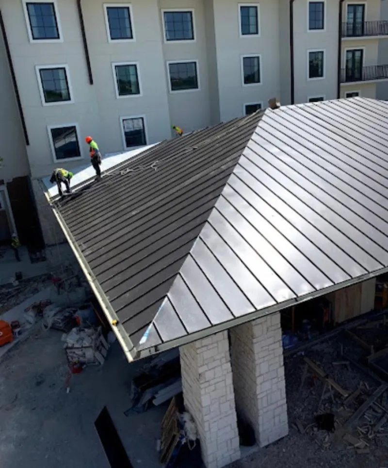 Crew installing standing seam metal roof panels on a commercial project in Derry